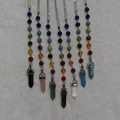 several necklaces with different colored stones hanging from chains on a white cloth covered surface