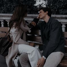 a man and woman sitting on a wooden bench talking to each other while holding hands