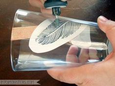 someone is using a stamper to cut out a feather on a clear glass bottle