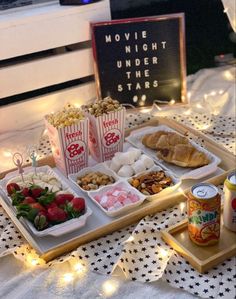 a table topped with trays filled with food and drinks next to a sign that says movie night under the stars