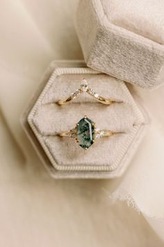 two gold rings with an oval cut green stone and diamond set in a velvet box