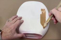 two hands holding a paintbrush and painting a white object with brown spots on it