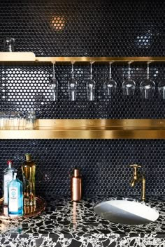 a bathroom with black tile and gold trim on the shelves, wine glasses are lined up next to each other