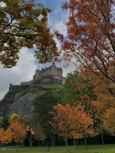 an old castle on top of a hill surrounded by trees with fall foliage in the foreground