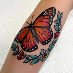 a butterfly tattoo on the arm with flowers and leaves around it's wings is shown