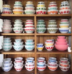 many bowls are stacked on top of each other in front of a wooden shelf filled with dishes