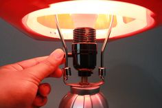 a hand is pointing at the light on top of a table lamp that has a microphone attached to it