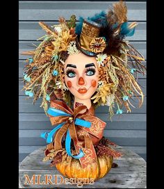 a close up of a doll with feathers on it's head and an orange pumpkin