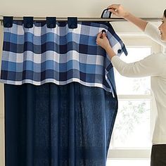 a woman is hanging a blue and white checkered curtain