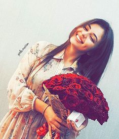 a woman holding a bunch of red roses in her right hand and smiling at the camera