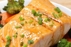 a white plate topped with salmon and broccoli on top of a wooden table