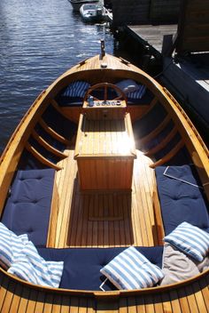 the inside of a wooden boat with blue cushions on it's deck and water in the background