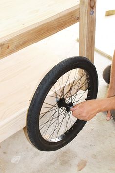 a man working on a bicycle wheel with wood and plywood in the back ground