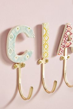 three metal hooks with letters on them hanging from the side of a pink wall next to each other