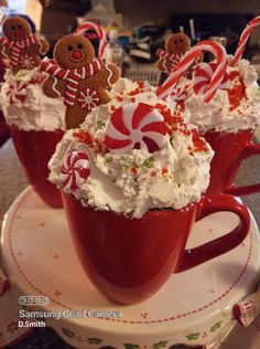 three red mugs filled with whipped cream and candy canes on top of a table