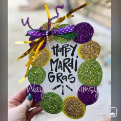 a hand holding up a mardi gras ornament that says happy mardi gras