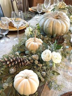 the table is set with white pumpkins, greenery and pine cones for centerpieces