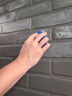 a person's hand holding a sponge against a brick wall with grey paint on it