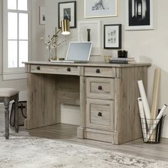 a desk with a laptop on top of it in front of pictures and framed photos