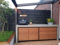 an outdoor kitchen with wooden cabinets and potted plants on the counter top, next to a brick wall