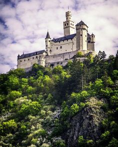 an old castle on top of a hill surrounded by trees and clouds in the sky