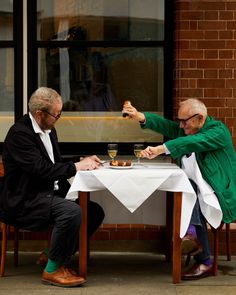 two men sitting at a table eating food and drinking wine