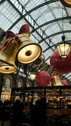 several lights hanging from the ceiling in a building with people walking around them and other items on display