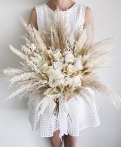 a woman holding a bouquet of white flowers and pamodia in her hands, against a gray background