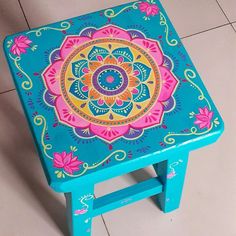 a blue stool with a colorful flower design painted on the top and bottom, sitting on tile flooring