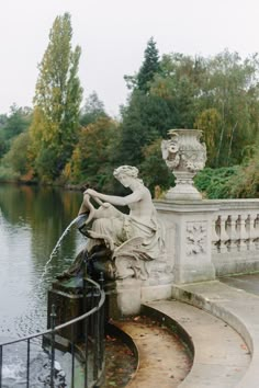 a fountain with a statue sitting on it's side next to a body of water