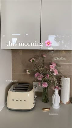 a white toaster sitting on top of a counter next to vases and flowers