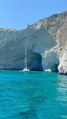 two boats in the water near a large white rock formation and blue water with cliffs on either side