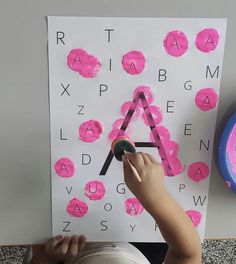 a young child is painting the letters on a white paper with pink crayons