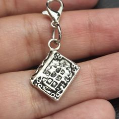 a hand holding a silver charm with a square design on it's side and a heart in the middle