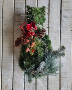 a christmas wreath hanging on the side of a wooden fence with pine cones, holly and poinsettis