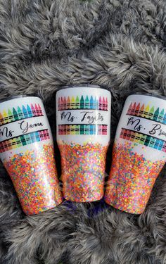 three cups with different colored sprinkles on them sitting on a furry surface