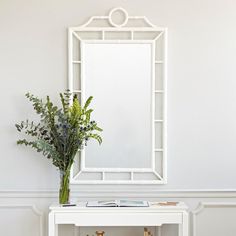 a white table with a vase and mirror on it