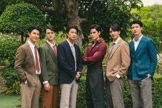 a group of young men standing next to each other in front of a green tree