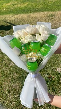 a bouquet of white roses wrapped in green and white paper with some beer cans on it