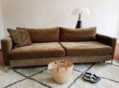 a brown couch sitting on top of a white rug next to a basket and lamp