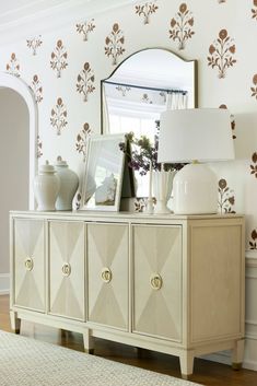 a white dresser sitting next to a mirror on top of a hard wood floor covered in furniture