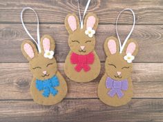 three felt easter bunnies hanging from strings on a wooden surface with flowers in their ears