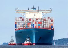 two tug boats in front of a large container ship