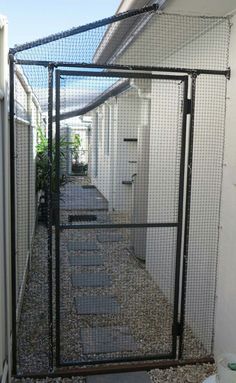 a black gate in front of a white building with gravel on the ground and plants behind it