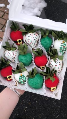 a hand holding a box full of chocolate covered strawberries with green and red decorations