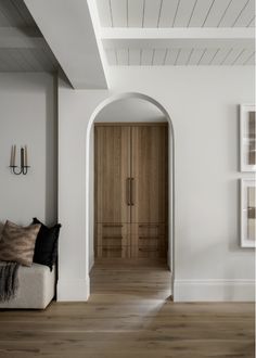 a living room with white walls and wooden floors, an archway leading to the bedroom