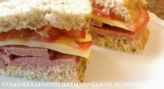 two sandwiches with meat, cheese and tomato on them sitting on a white platter