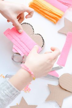 someone cutting out paper hearts with scissors on top of a white table covered in pink and orange strips