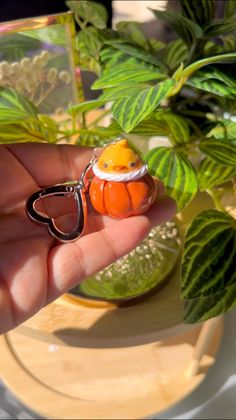 a hand holding an orange bird shaped keychain in front of a potted plant