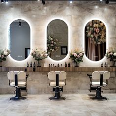 there are three chairs in the room with mirrors on the wall and flowers behind them